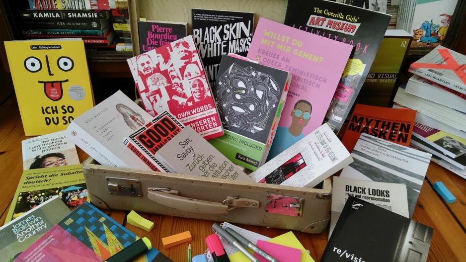 Arbeitskoffer Diversitätskompetenz In einem aufgeklappten Koffer finden sich viele Bücher zu Diversität, vor dem Koffer liegen Textmarker und Post-Its